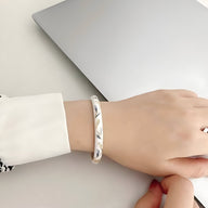 Bracelet jonc en cuivre plaqué or avec motif fleuri scintillant porté au poignet, finition brillante.