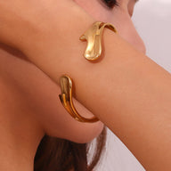 Bracelet jonc doré en acier inoxydable avec silhouette fluide et design moderne porté au poignet.