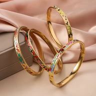 Quatre bracelets joncs dorés émaillés avec motifs géométriques colorés sur fond beige satiné.