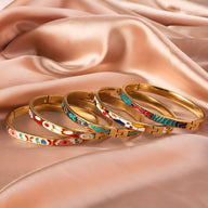 Bracelets joncs en métal doré avec motifs émaillés colorés variés posés sur tissu satin saumon.