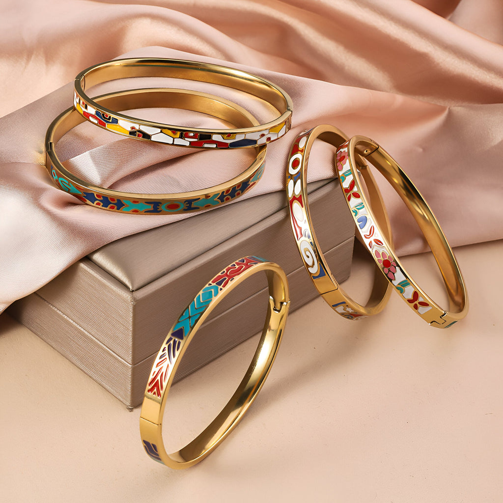 Lot de cinq bracelets joncs dorés émaillés avec motifs colorés variés sur fond beige satiné.