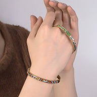 Bracelet jonc émaillé vert avec motifs colorés porté sur poignet féminin, style élégant et fin.