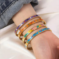 Bracelets joncs fins en métal doré avec émail coloré aux motifs variés, portés au poignet.