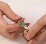 Bracelet jonc doré avec émail vert et motifs géométriques jaunes et rouges, porté aux mains féminines.