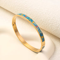 Bracelet jonc en métal doré avec émail turquoise décoré de petits motifs colorés rouges et blancs.