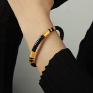 Bracelet jonc en titane noir avec détails dorés, design fin et élégant pour femme.