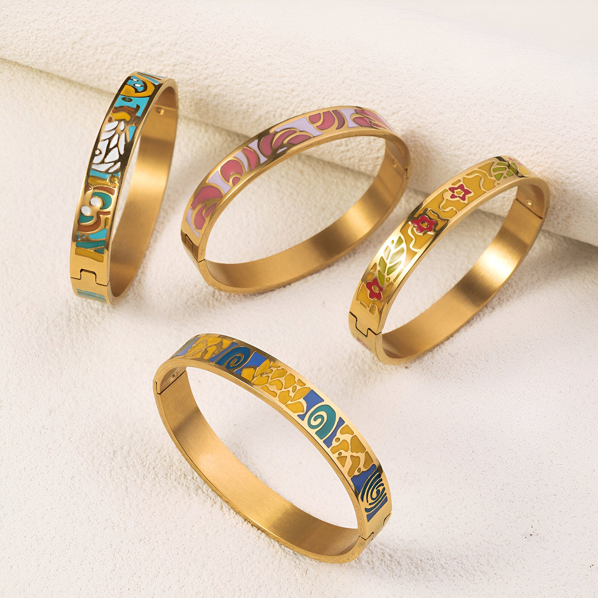 Quatre bracelets joncs dorés émaillés avec motifs floraux et géométriques colorés délicats.