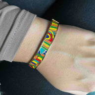 Bracelet jonc en métal doré avec émail coloré motif abstrait multicolore porté au poignet.