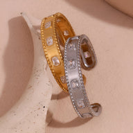 Bracelet jonc ouvert en acier inoxydable or et argent avec pierres carrées incrustées et bordure texturée.