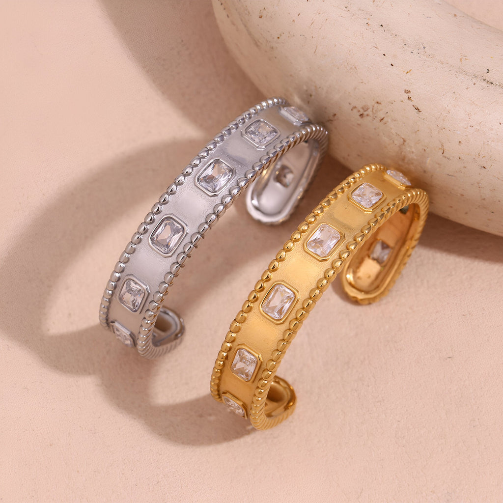 Bracelet jonc en acier inoxydable or orné de pierres carrées ajourées avec bords perlés, modèle Sohan et version argentée.