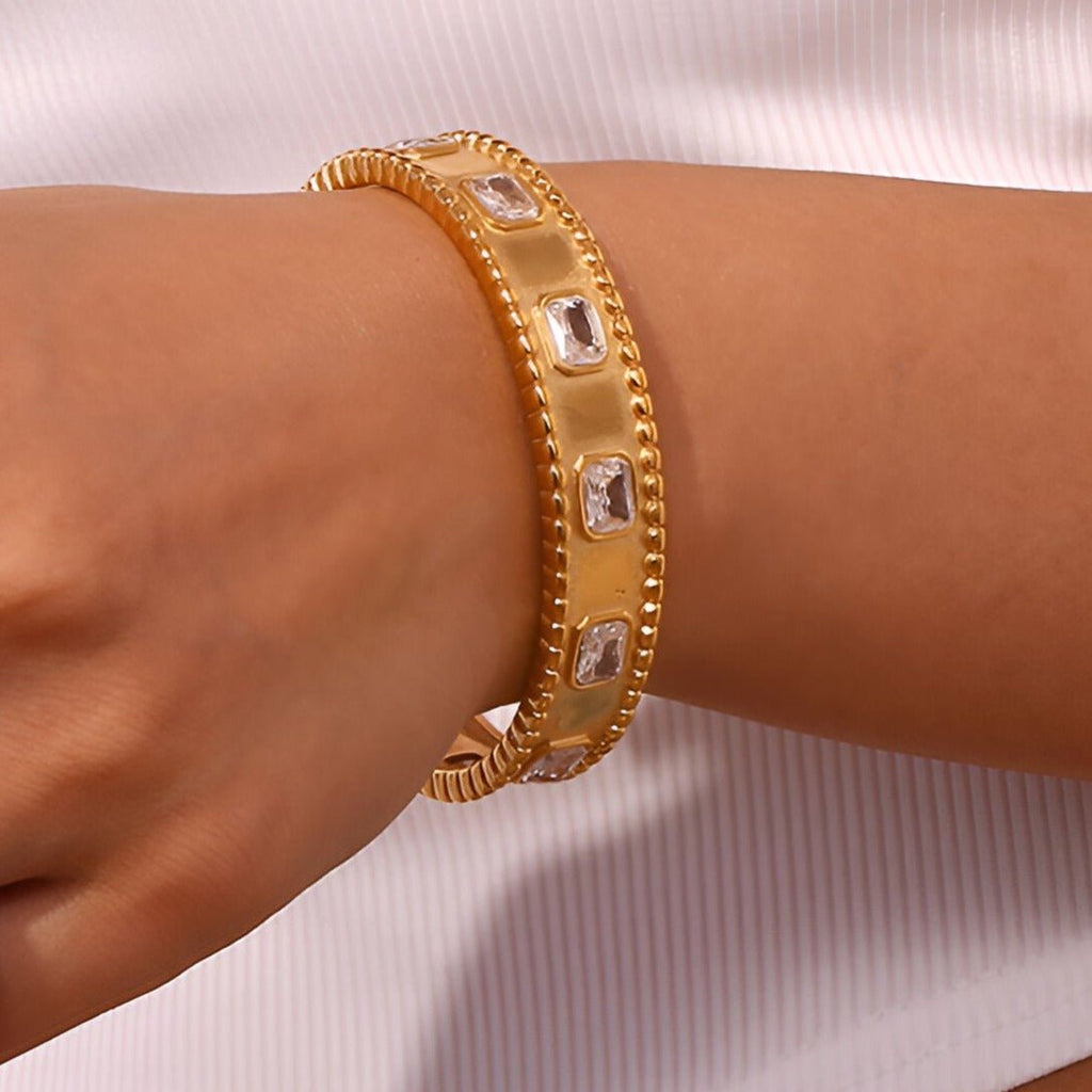 Bracelet jonc doré en acier inoxydable avec pierres carrées et détails texturés.