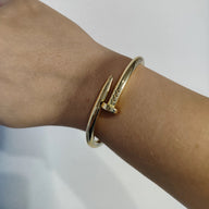 Bracelet jonc doré en acier inoxydable avec extrémités en forme de clou sur poignet féminin.