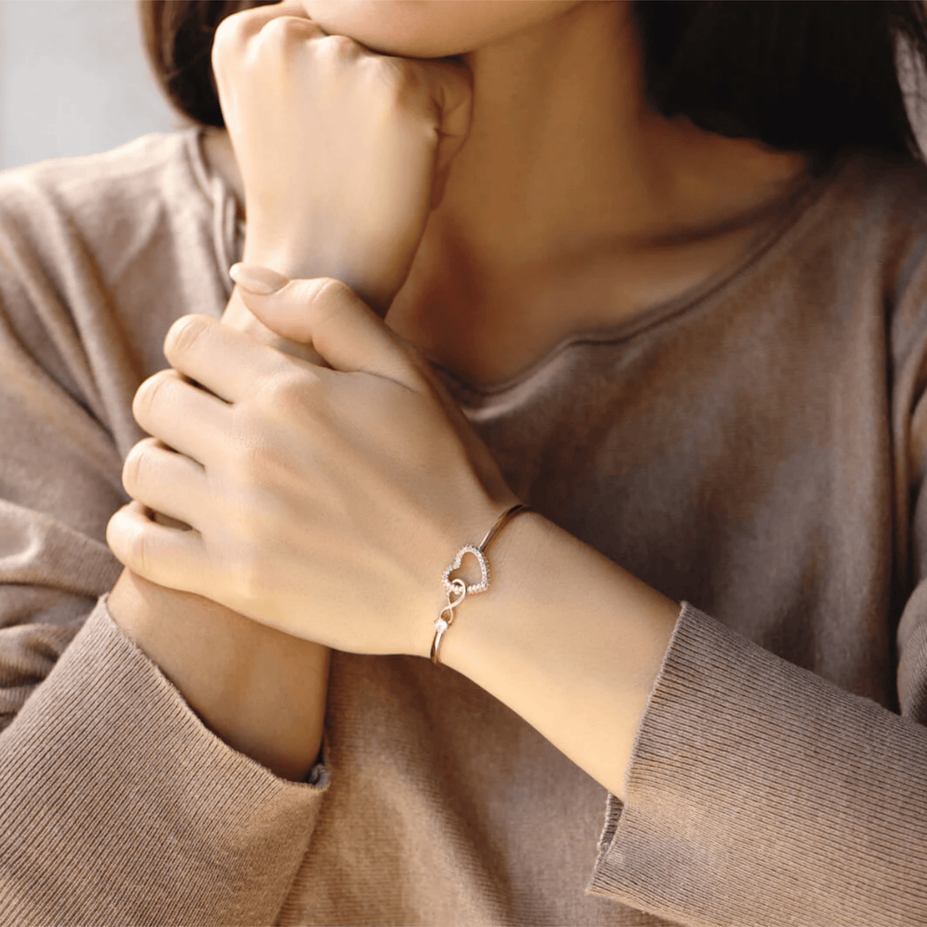 Bracelet jonc plaqué or en acier inoxydable avec pendentif cœur infini orné d'une pierre zircon claire, porté au poignet.