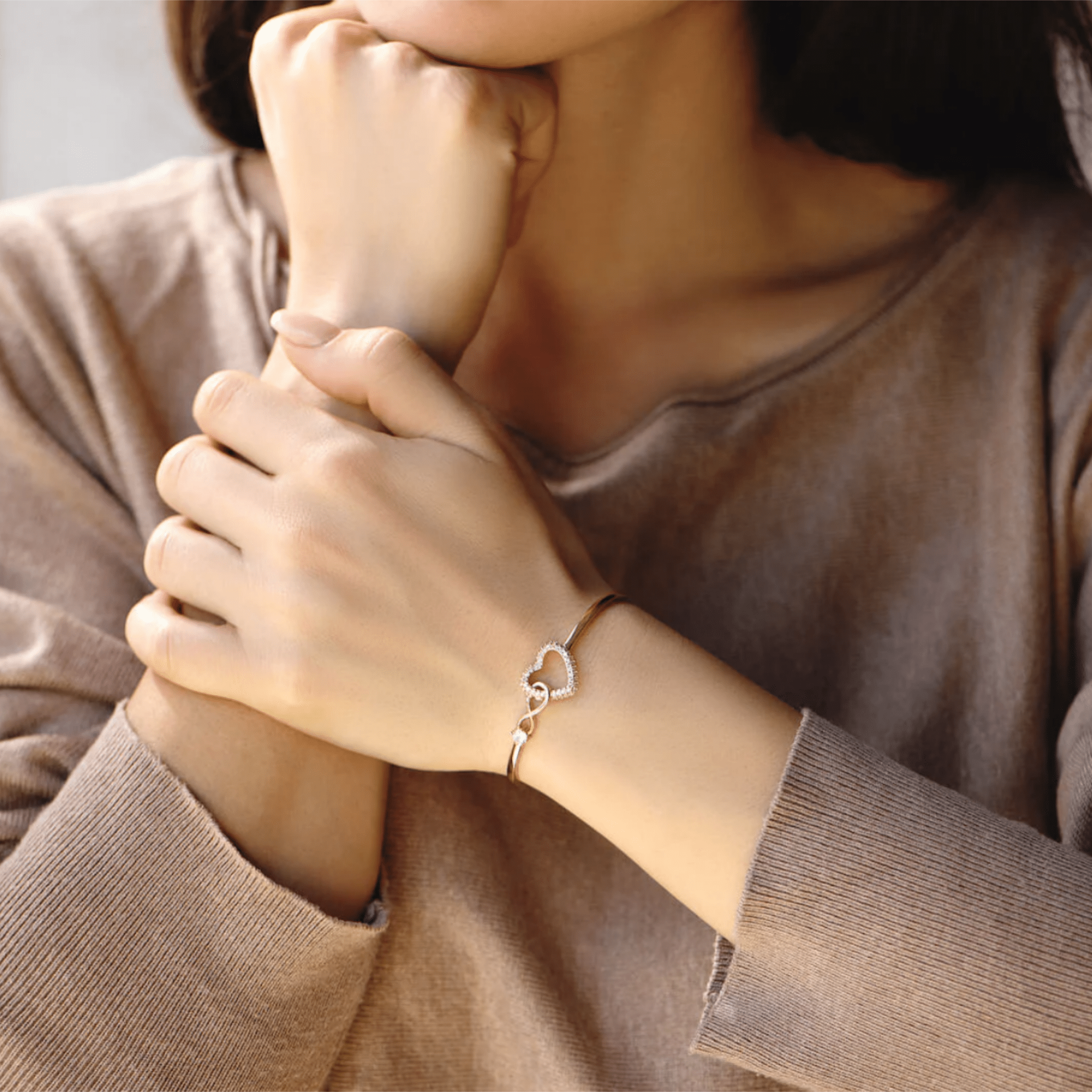 Bracelet jonc plaqué or en acier inoxydable avec pendentif cœur infini orné d'une pierre zircon claire, porté au poignet.