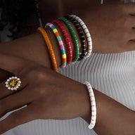 Bracelets jonc colorés en titane et acrylique empilés sur un poignet, avec un bracelet blanc séparé porté sur l'autre poignet.