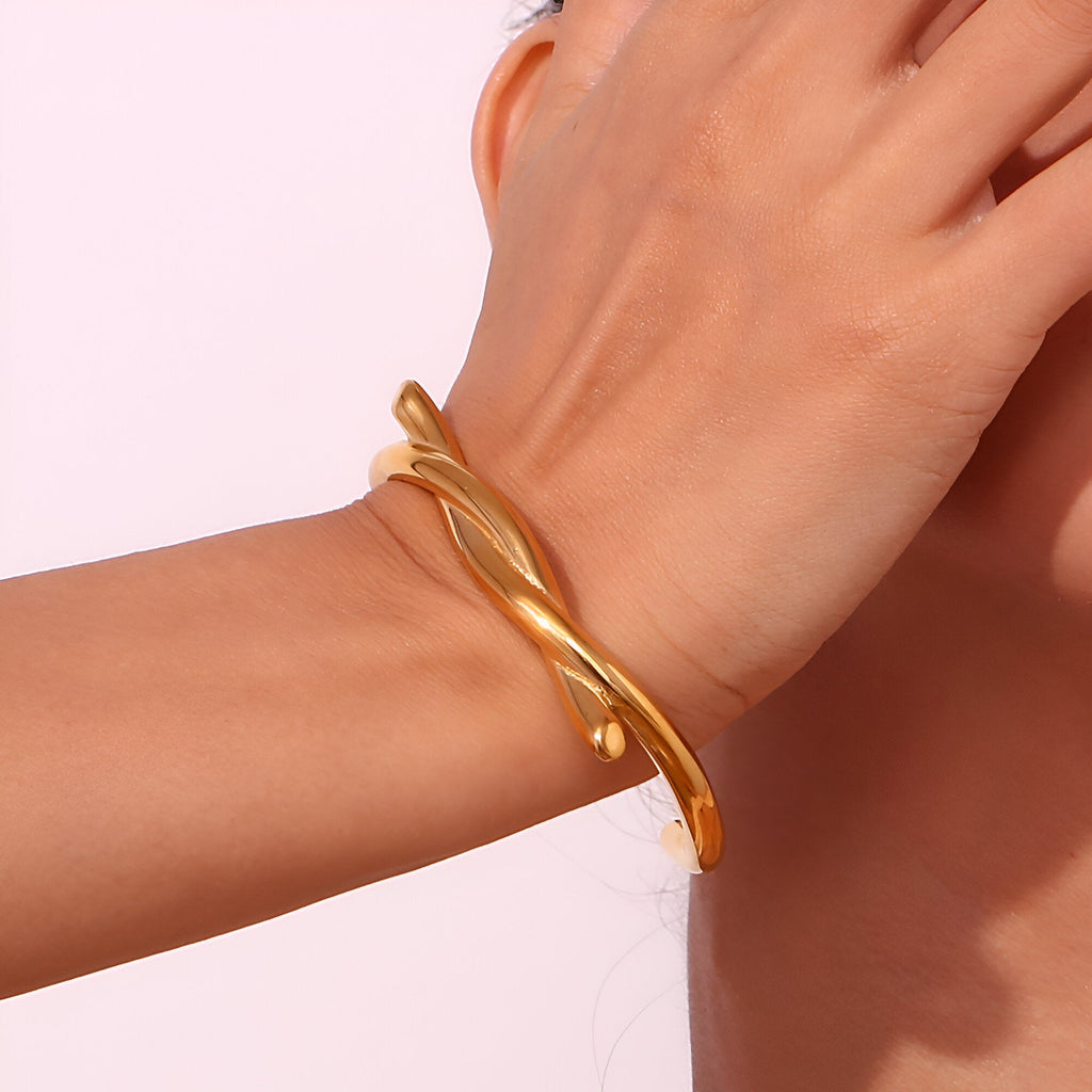 Bracelet jonc en acier inoxydable doré avec demi nœud élégant sur poignet féminin.