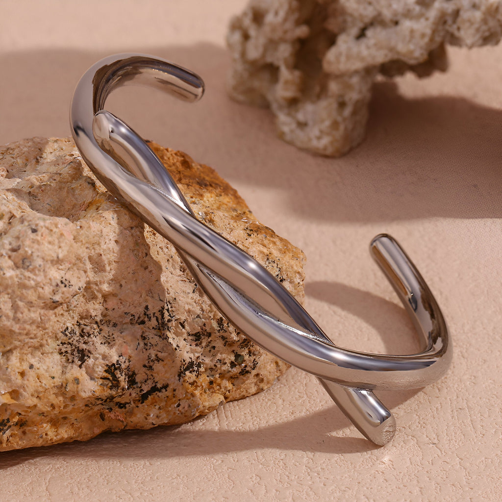 Bracelet jonc demi nœud en acier inoxydable argenté modèle Amara posé sur roche beige.