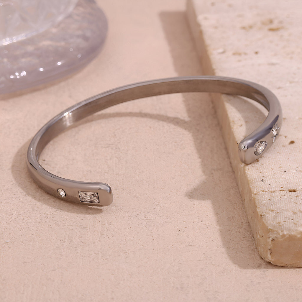 Bracelet jonc en acier inoxydable argenté avec petits motifs gravés aux extrémités.