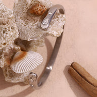 Bracelet jonc fin en acier inoxydable argenté avec motifs astres gravés et strass subtils.