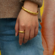 Bracelet jonc fin doré en acier inoxydable gravé de motifs astres porté au poignet, bague assortie au doigt.