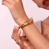 Bracelet jonc doré en acier inoxydable avec design entrelacé, finition lisse et brillante.