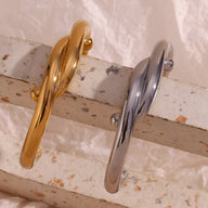 Bracelet jonc entrelacé en acier inoxydable finition or brillant et argenté posé sur surface texturée beige.