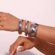 Lot de trois bracelets joncs en acier inoxydable argenté au design épuré sur un poignet.