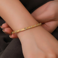 Bracelet jonc fin en acier inoxydable doré avec motif géométrique et petits cristaux scintillants.