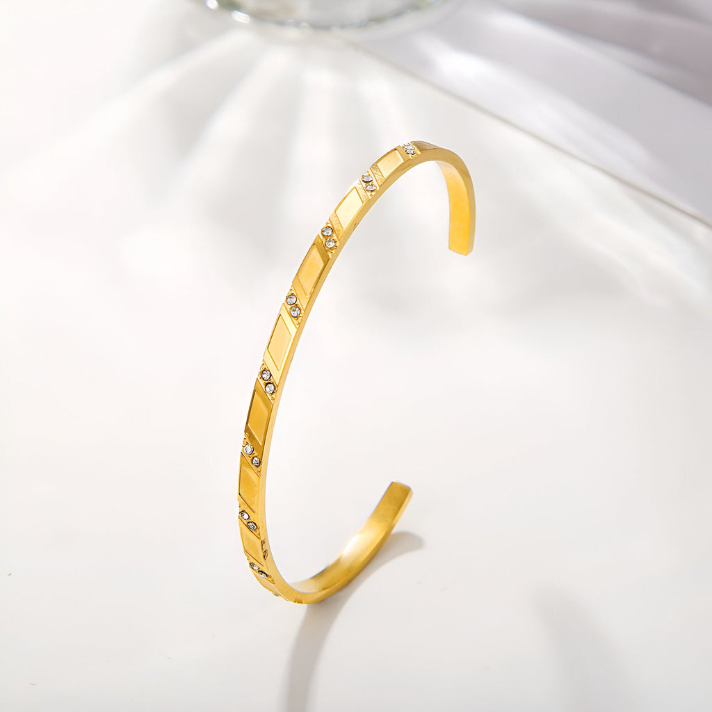 Bracelet jonc fin en acier inoxydable doré orné de motifs géométriques ajourés et petits clous brillants.