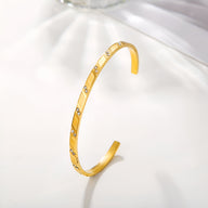 Bracelet jonc fin en acier inoxydable doré orné de motifs géométriques ajourés et petits clous brillants.