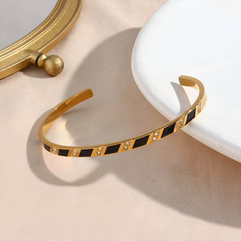 Bracelet jonc doré en acier inoxydable avec motif géométrique noir et détails carrés brillants.