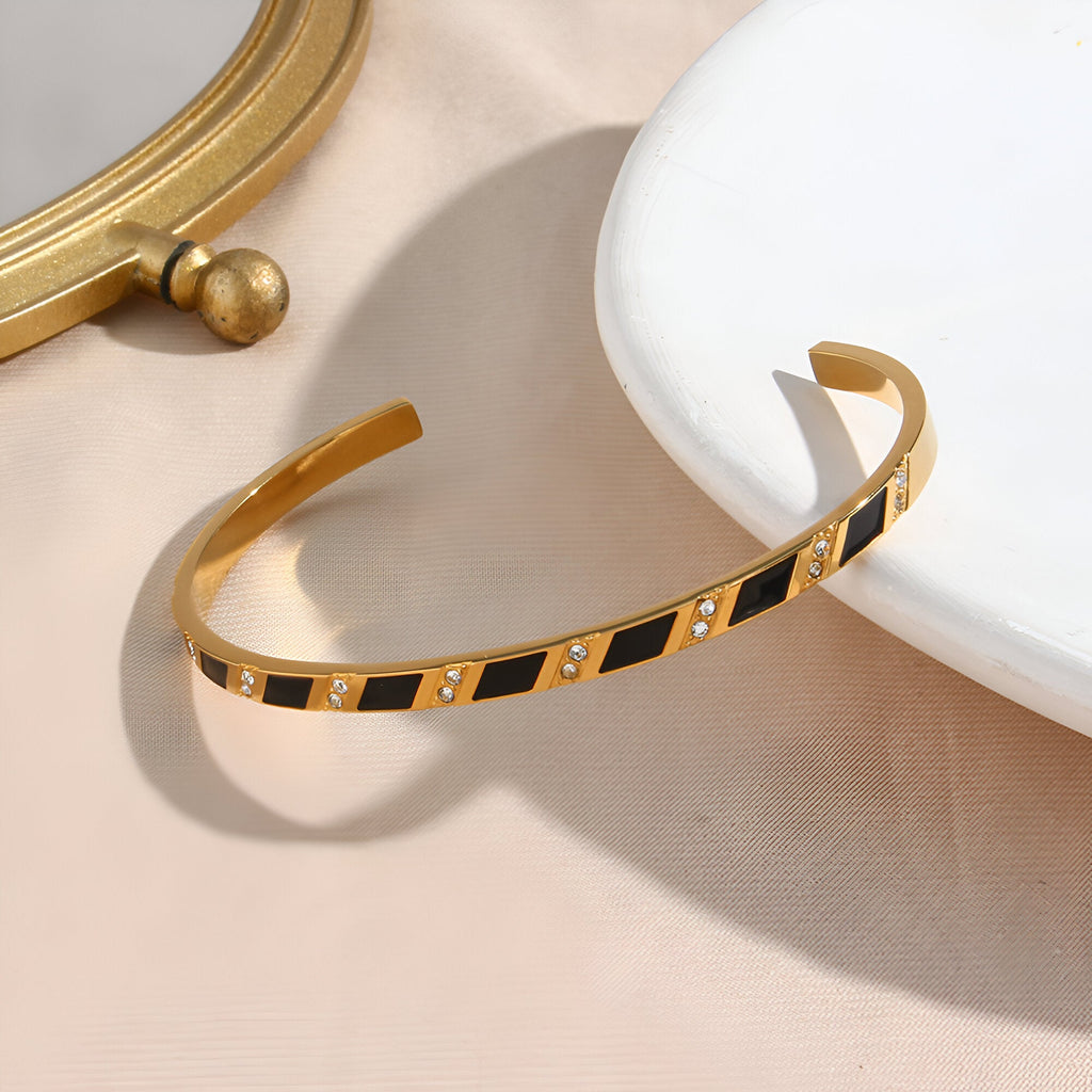 Bracelet jonc doré en acier inoxydable avec motif géométrique noir et détails carrés brillants.