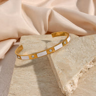 Bracelet jonc doré en acier inoxydable avec motifs géométriques blancs et incrustations de pierres brillantes.