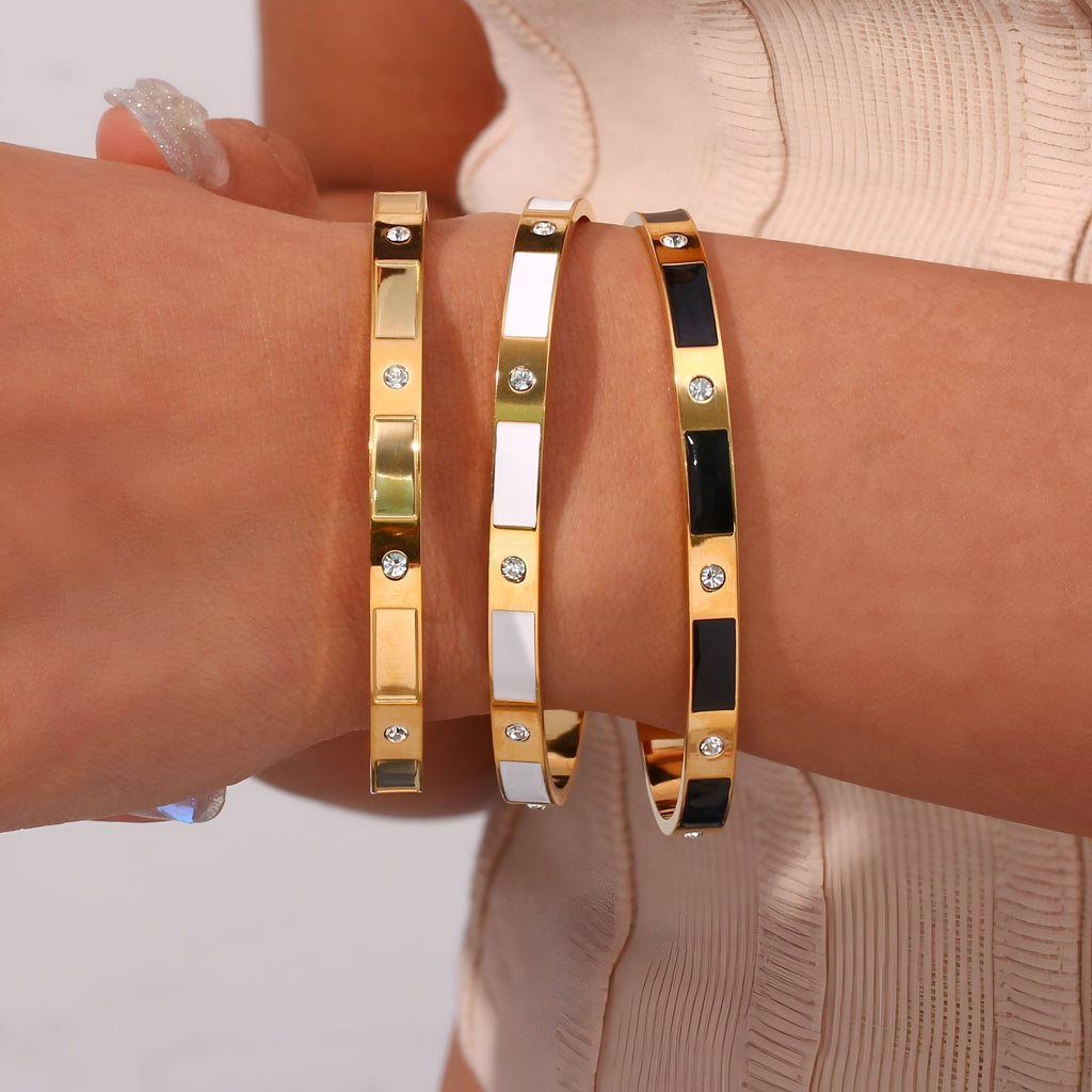 Trois bracelets joncs en acier inoxydable or, blanc et noir avec détails géométriques et strass.