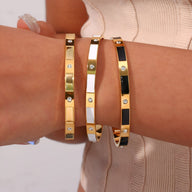 Trois bracelets joncs en acier inoxydable or, blanc et noir avec détails géométriques et strass.