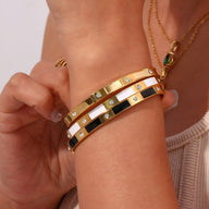 Bracelet jonc en acier inoxydable or avec motifs géométriques carrés ponctués de strass blancs et noirs.