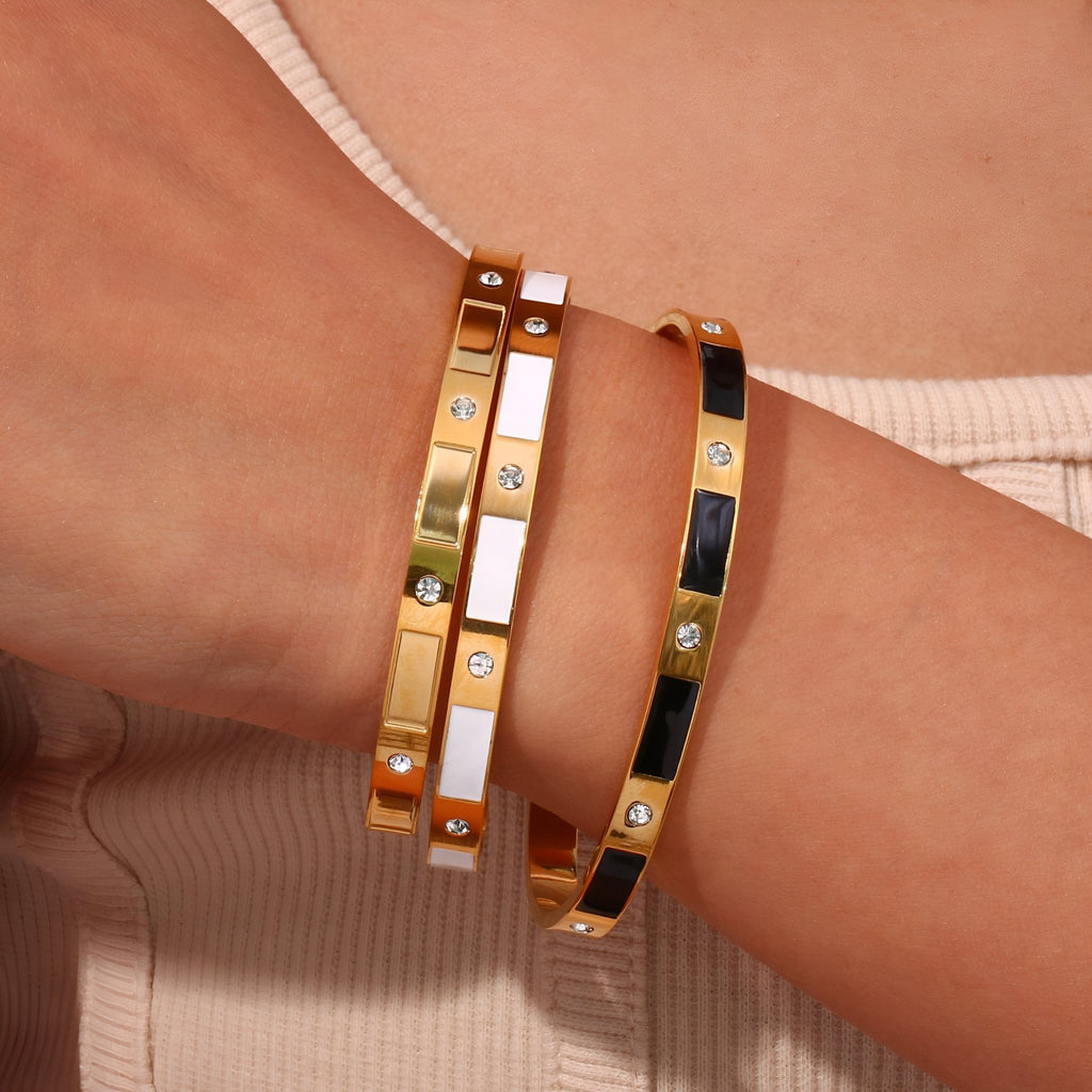 Bracelet jonc en acier inoxydable or avec motifs géométriques et incrustations de pierres sur poignet féminin.