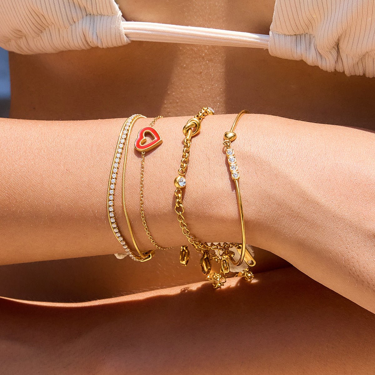 Bracelet jonc doré 18 carats avec cœur rouge et zircons scintillants, fermoir mousqueton, ajustable, porté au poignet.