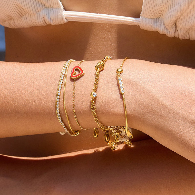 Bracelet jonc doré 18 carats avec cœur rouge et zircons scintillants, fermoir mousqueton, ajustable, porté au poignet.