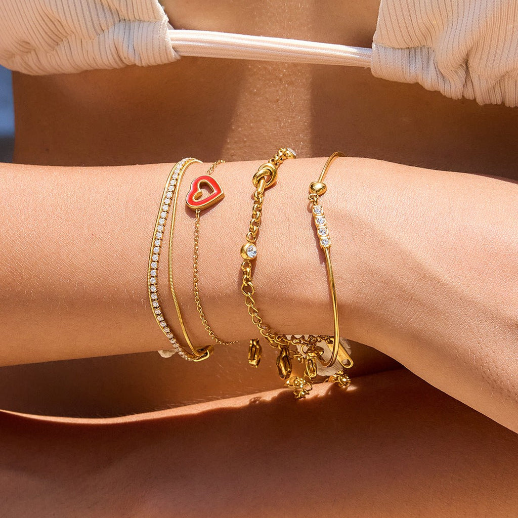 Bracelet jonc doré 18 carats avec cœur rouge et zircons scintillants, fermoir mousqueton, ajustable, porté au poignet.