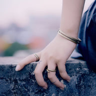 Bracelet jonc double en cuivre or vieux autour du poignet, accompagné de deux bagues fines assorties sur les doigts.