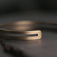 Bracelet jonc double en cuivre or vieux avec finition brossée et design ajouré rectangulaire.