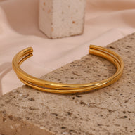 Bracelet jonc duo torsadé en acier inoxydable finition or brillant posé sur pierre texturée.