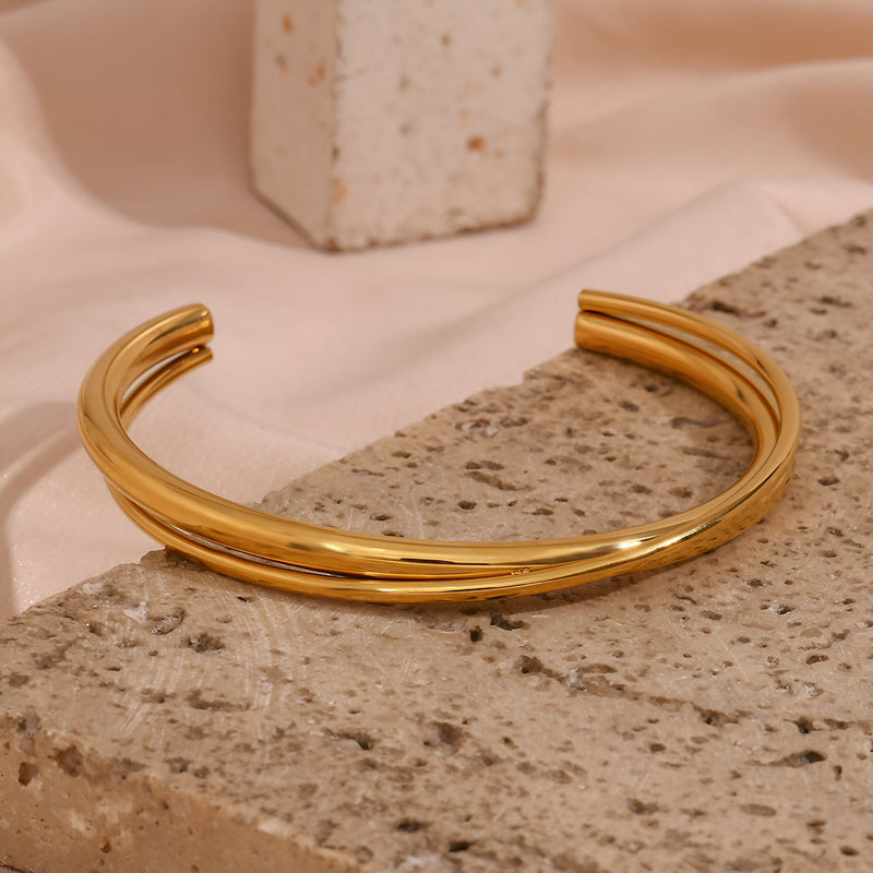 Bracelet jonc duo torsadé en acier inoxydable finition or brillant posé sur pierre texturée.