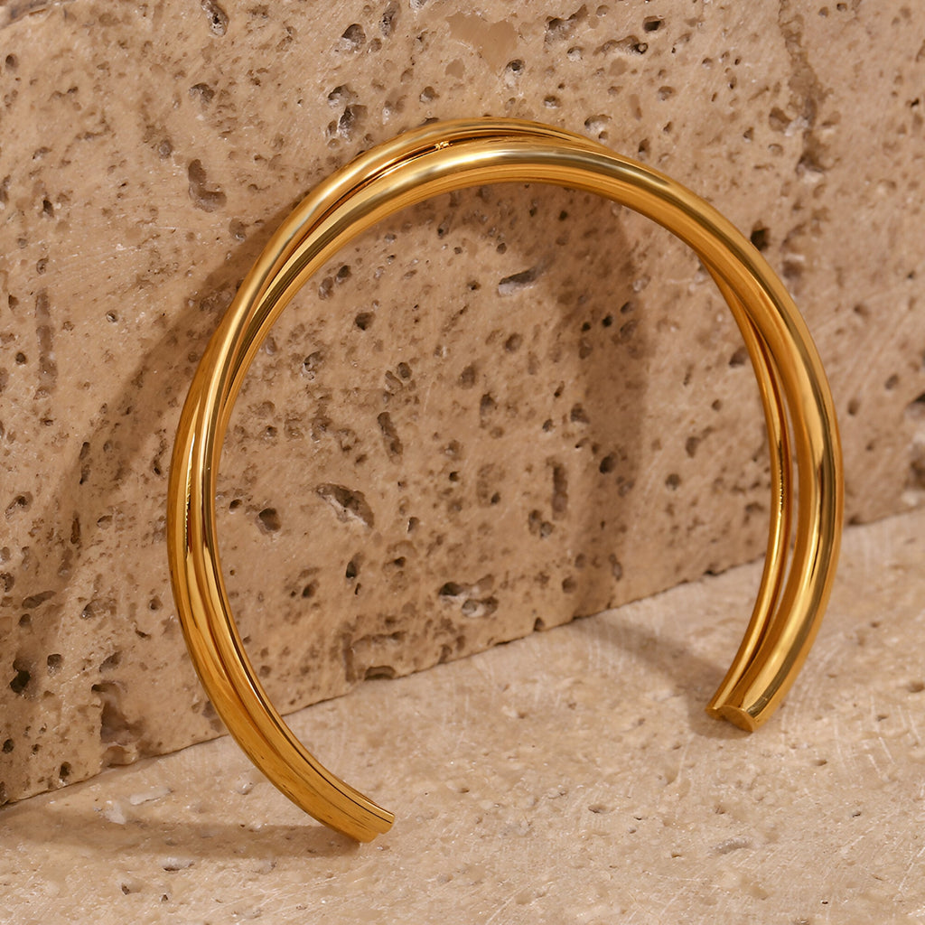 Bracelet jonc duo torsadé en acier inoxydable couleur or brillant sur fond pierre beige.