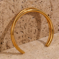 Bracelet jonc duo torsadé en acier inoxydable couleur or brillant sur fond pierre beige.