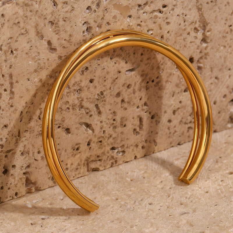 Bracelet jonc duo torsadé en acier inoxydable couleur or brillant sur fond pierre beige.