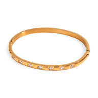 Bracelet jonc doré en acier inoxydable avec inserts en cristaux brillants, design fin et élégant.