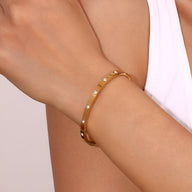 Bracelet jonc fin en acier inoxydable doré avec éclats lumineux sur poignet féminin.