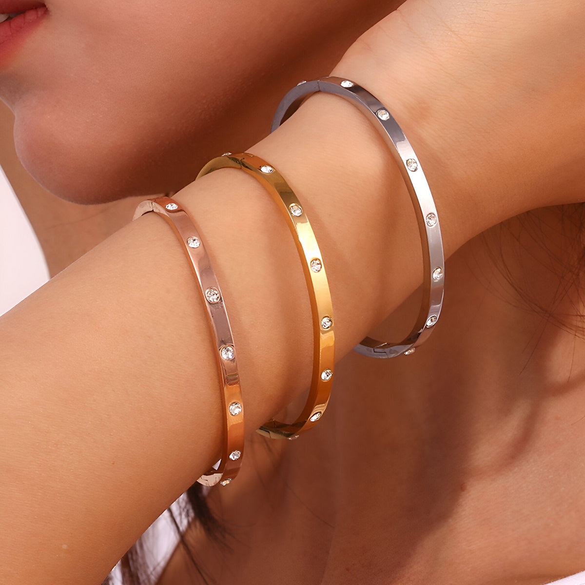 Trois bracelets joncs Roshan en acier inoxydable, finitions or, or rosé et argent, décorés de petits éclats lumineux.
